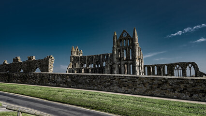 Obraz premium Whitby Abbey's ruins standing tall against a vibrant blue sky in the picturesque North York Moors National Park, UK