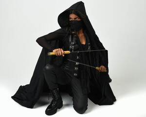 full body portrait of confident brunette woman wearing black leather costume and cape, holding...