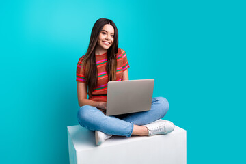 Naklejka premium Young woman sitting with a laptop in a casual outfit against a teal background