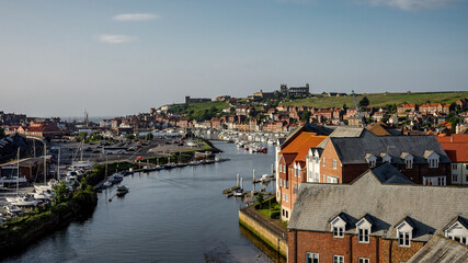 Obraz premium Scenic view of Whitby harbor in North Yorkshire, featuring Saint Mary's Church and boats on the River Esk on a sunny summer day