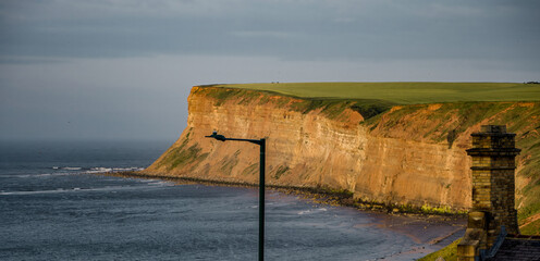 Dramatic sunset light illuminating the cliffs at Saltburn by the Sea, UK, with a street lamp and chimney adding interest to the foreground