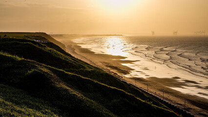 Breathtaking view of Saltburn beach during a golden sunset, with offshore wind turbines and grassy cliffs creating a serene coastal landscape