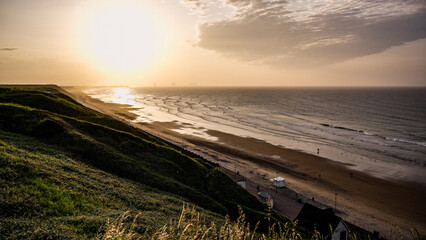 Beautiful sunset reflecting on north sea waves rolling on Saltburn sandy beach at low tide with grassy cliff in foreground, United Kingdom
