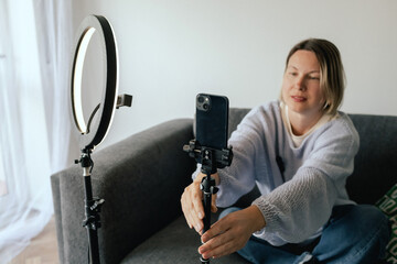 Middle-aged woman beauty blogger filming skincare product unboxing at home with ring light....