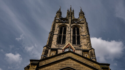 Low angle view of St. Nicholas Cathedral's tower and clock, with a cloudy sky in the background, in Newcastle upon Tyne