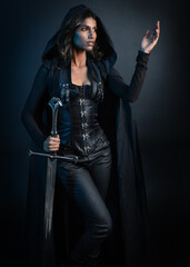 portrait of mysterious hooded woman in black cloak, gothic fantasy or dystopian character, holding sword weapon. lit with moody cinematic shadows, studio scene on dark isolated background