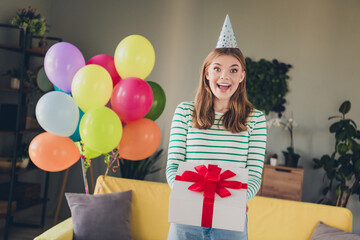 Young woman celebrating with balloons and a gift in a cozy living room on her birthday