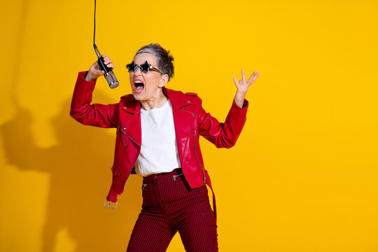 Energized senior woman singing passionately with a microphone against a vibrant yellow background