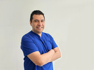 A dark-skinned Latino male doctor wearing blue surgical scrubs works in a hospital and appears successful, productive and hardworking