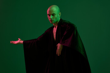 A focused man in a flowing robe strikes a confident pose against an abstract green background,...