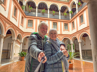 Smiling senior couple takes a selfie together on the patio of a historic house in Seville during a sightseeing trip enjoying the culture and the pleasant retirement lifestyle