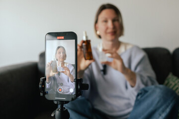 Middle-aged woman beauty blogger filming skincare product unboxing at home with ring light....