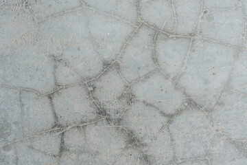 A close-up view of a cracked concrete surface, showcasing irregular fissures and the texture of the...