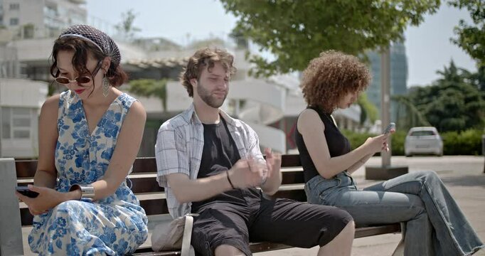 Three friends sit on a bench, each engrossed in their smart phones, seemingly ignoring each other.