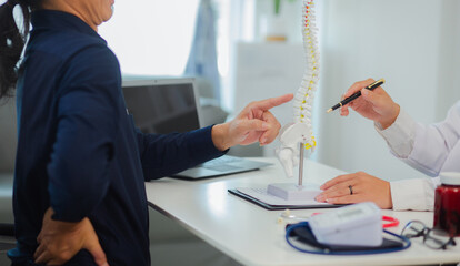An orthopedic doctor shows a spinal model to a patient in a human spinal hospital. Diseases and disorders of the spinal cord, back pain, lumbar pain, orthopedic surgery, chiropractic, office syndrome
