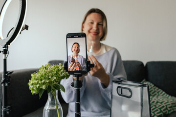Middle-aged woman beauty blogger filming skincare product unboxing at home with ring light....