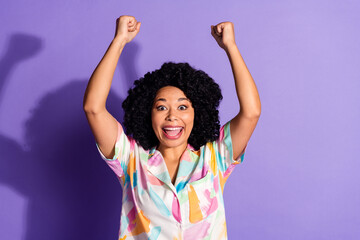 Joyful woman in colorful shirt celebrates with raised arms against vibrant purple backdrop,...