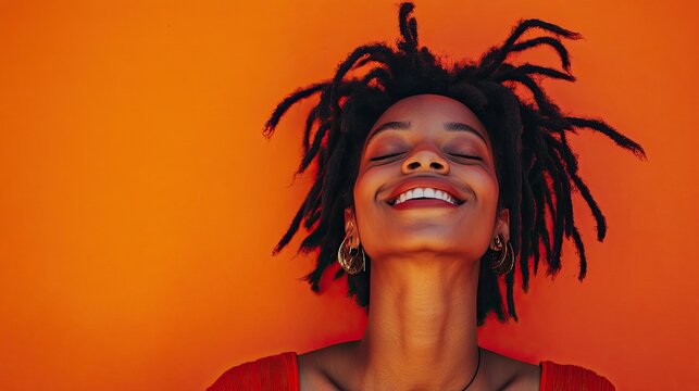 A joyful woman with long, flowing dreadlocks dances against a vibrant orange background.