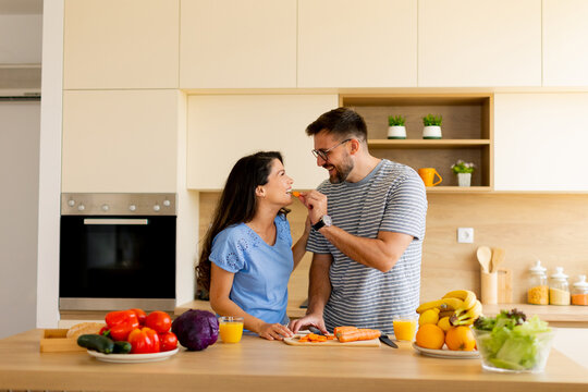 Joyful couple sharing healthy meal prep in a modern kitchen filled with fresh produce during a sunny afternoon - Powered by Adobe