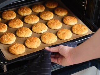 Woman taking baking tray with tasty curd cheese pancakes (syrniki) out of the oven