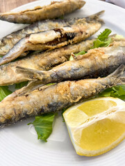 Fried fish served with fresh lemon on a white plate with greens at a seaside restaurant during a sunny afternoon