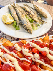 Freshly fried sardines with crispy potatoes topped with sauce served at a sunny outdoor cafe in a coastal town