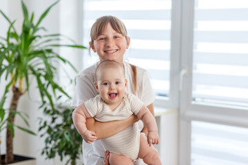 Smiling sister holding laughing baby indoors