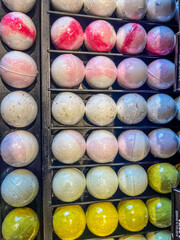 Vibrant selection of handcrafted bath bombs displayed in a wooden tray at a local artisan market in...