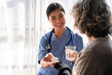 Asian Nurse Helping Older Woman with Medication and Water Glass in Home Healthcare Setting Ensuring Wellness and Treatment Plan