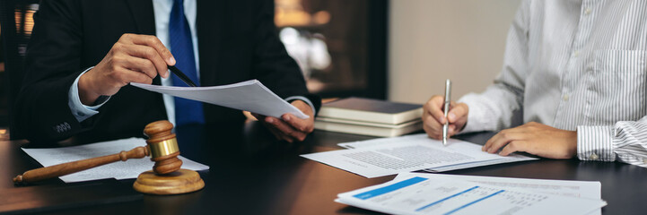 Two people are sitting at a desk with papers and a gavel
