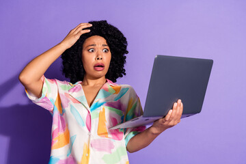 Young woman surprised while looking at laptop against vibrant purple background in stylish colorful...