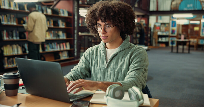 Student, laptop and typing in library with man for studying, assignment or thesis on college campus. Computer, writing and male person with education, preparation for exam or research for paper - Powered by Adobe