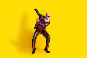 Naklejka premium Charismatic senior man dancing in vibrant suit against a bright yellow backdrop, radiating joy and style
