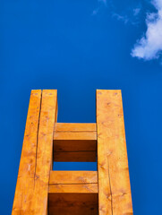 Wooden ladder reaching toward a bright blue sky with clouds, symbolizing a surreal stairway to...