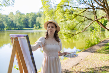 A female artist in a light dress and a straw hat, standing at an easel with a palette in her hands....