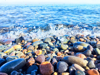 Colorful pebbles along the shoreline with waves crashing gently on a sunny day at the beach
