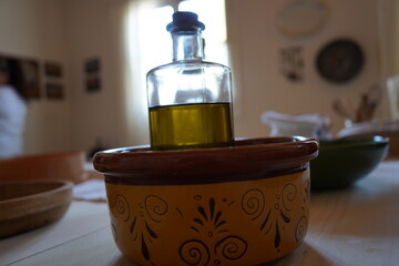 A clear glass bottle filled with olive oil sits atop a decorative yellow ceramic bowl with brown...