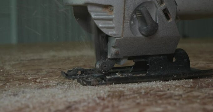 Close-up of a jigsaw cutting through oriented strand board, creating flying sawdust particles with professional skill. A man uses a jigsaw to cut through an osb sheet.