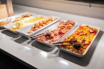 Variety of hot breakfast dishes on buffet table in hotel dining area. Morning meal options, protein-rich food, and colorful nutrition concept.