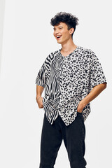 young man laughing in stylish black and white animal print shirt with hands in pockets against...