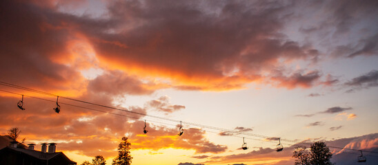 Scenic sunset view with vibrant orange and purple clouds, silhouetted ski lift cables, and distant mountains creating tranquil atmosphere for outdoor enthusiasts and nature lovers