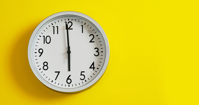 Time 1 minute to six or eighteen o'clock, round clock on yellow background. 5:59 or 17:59