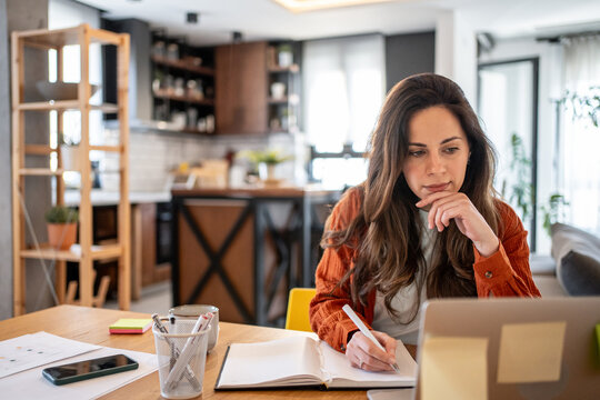 Focused freelancer working from home taking notes from laptop