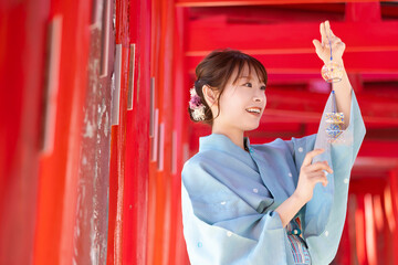 Japanese woman in yukata holding a wind chime in front of the red torii gate of the shrine