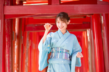 Japanese woman in yukata holding a wind chime in front of the red torii gate of the shrine