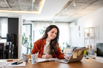 Freelancer working from home using laptop and taking notes