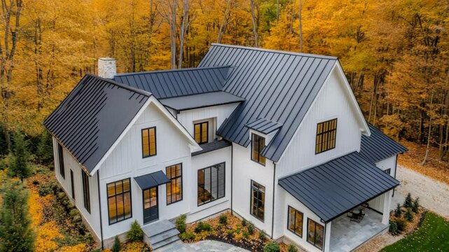 Aerial shot of modern farmhouse with white board and batten siding and black metal roof in autumn setting