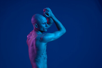 Male model posing gracefully against a vibrant blue backdrop, showcasing strong emotions and an artistic expression. Captured in a colorful light setting.
