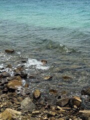 Photo of water and coastline in Asia. White sand, rocky bottom of the sea. The coral reef starts here. The water is turquoise and clear, there are small waves