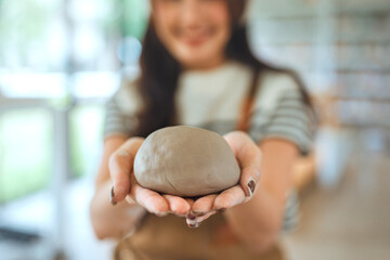 Close-up of asian woman’s hands holding raw clay before shaping pottery – beginning of handmade...